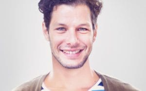 A man with brown hair and striped shirt smiling.