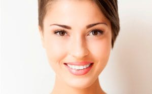 A woman with brown hair and pink lips smiles for the camera.