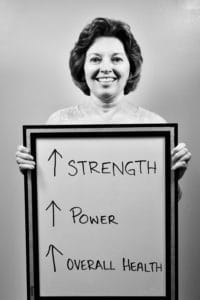 A woman holding up a sign with arrows pointing to the word strength.