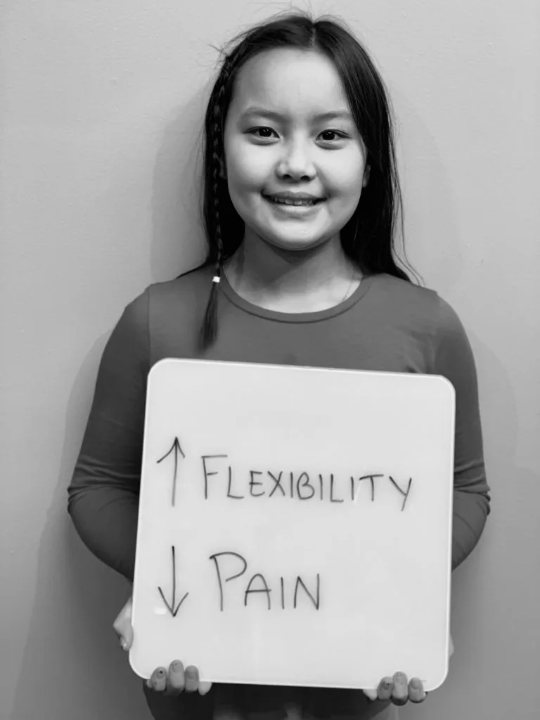 patient story - A young girl holding up a sign that says improved flexibility and reduced pain- neuro-structural chiropractic adjustment results for pediatrics