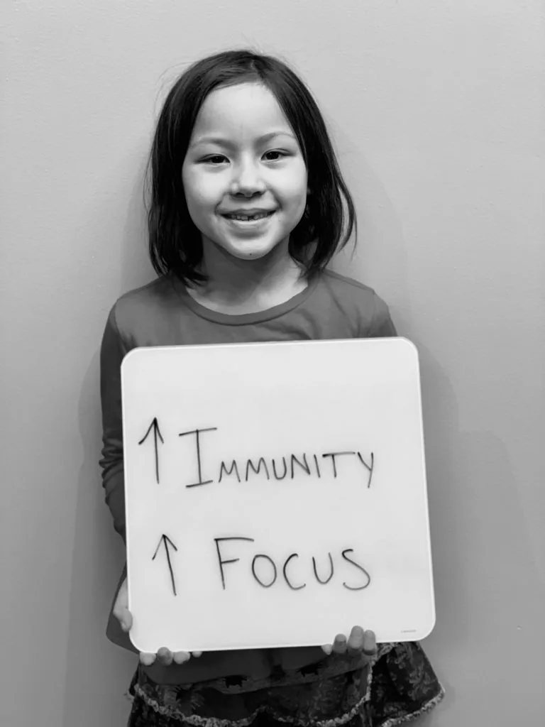 patient story - A young girl holding up a sign that says improved immunity and focus - neuro-structural chiropractic adjustment results for pediatrics