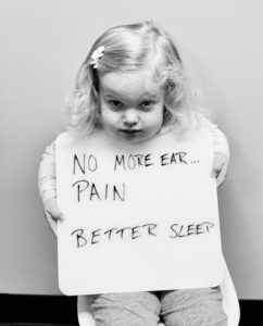 A little girl holding up a sign that says no more ear pain.