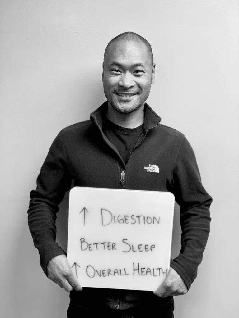patient story - A man holding up a sign that says better digestion, better sleep, and better overall health- neuro-structural chiropractic adjustment results for adults