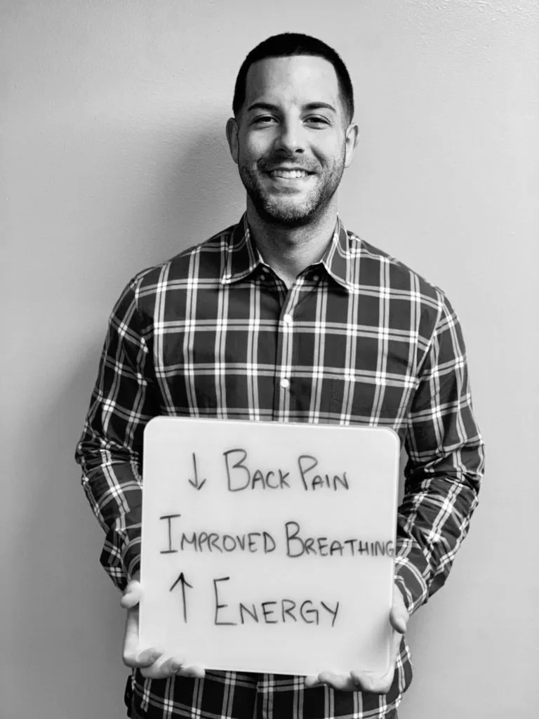 patient story - A man holding up a sign that says reduced back pain, improved breathing and energy- neuro-structural chiropractic adjustment results for adults