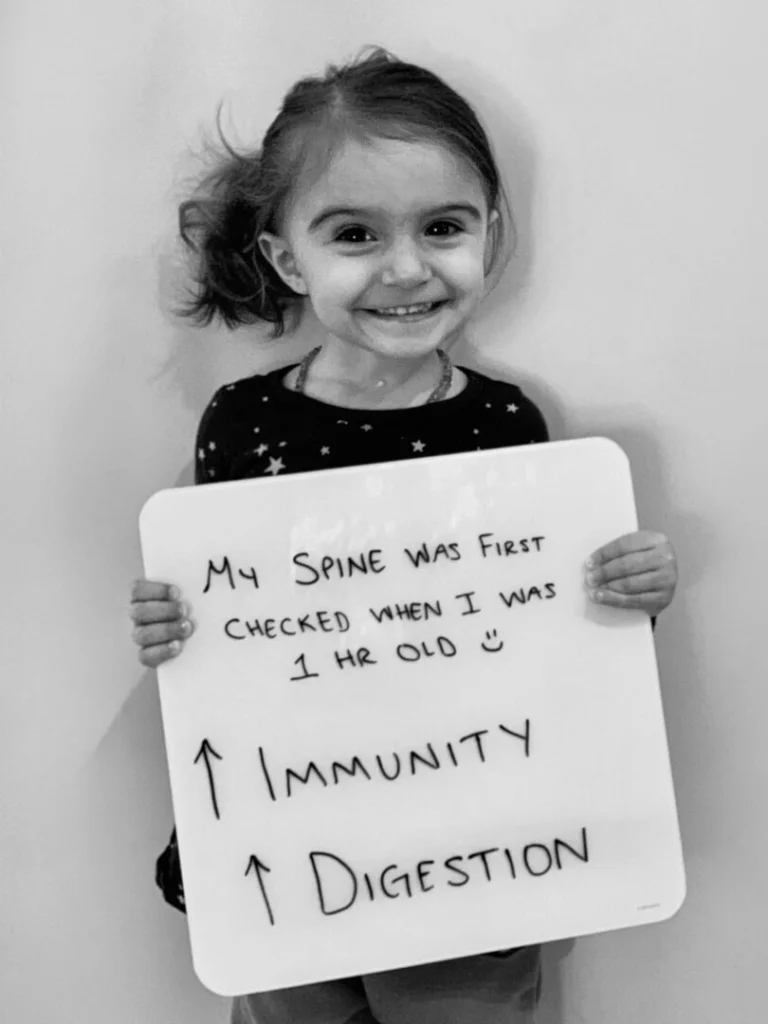 patient story - little girl holding a sign that says improved immunity and digestion - neuro-structural chiropractic adjustment results for children