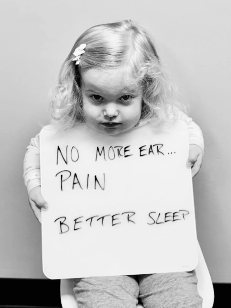 patient story - little girl holding a sign that says no more ear pain and better sleep - neuro-structural chiropractic adjustment results for children