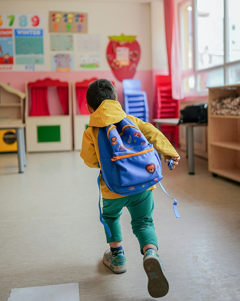 child wearing a heavy backpack running into a classroom - pediatric Chiropractic care