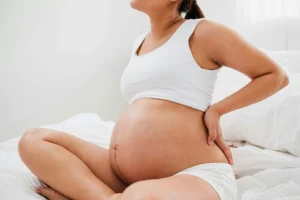 pregnancy and perinatal chiropractic care - pregnant woman sitting on the bed holding her back
