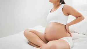 pregnancy and perinatal chiropractic care - pregnant woman sitting on the bed holding her back