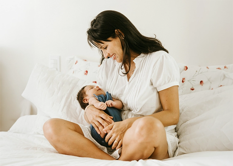 woman sitting on the bed holding her newborn baby - chiropractic care for pregnancy and postpartum recovery